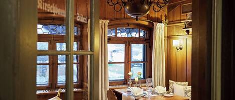 Un comedor acogedor con paredes de madera, una araña y vistas a un paisaje nevado a través de amplios ventanales.