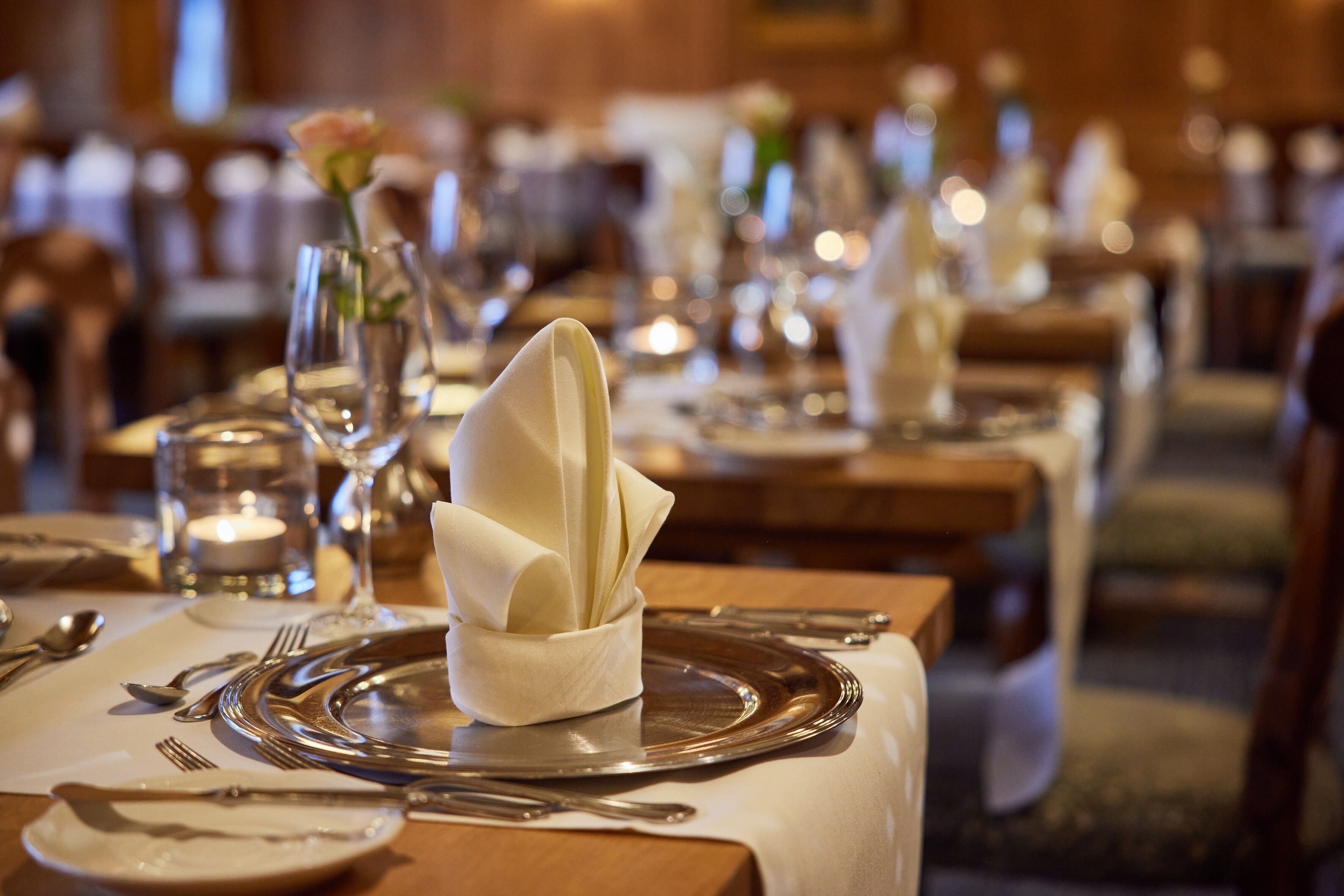 A dining table set with a folded napkin, silverware, and a glass.