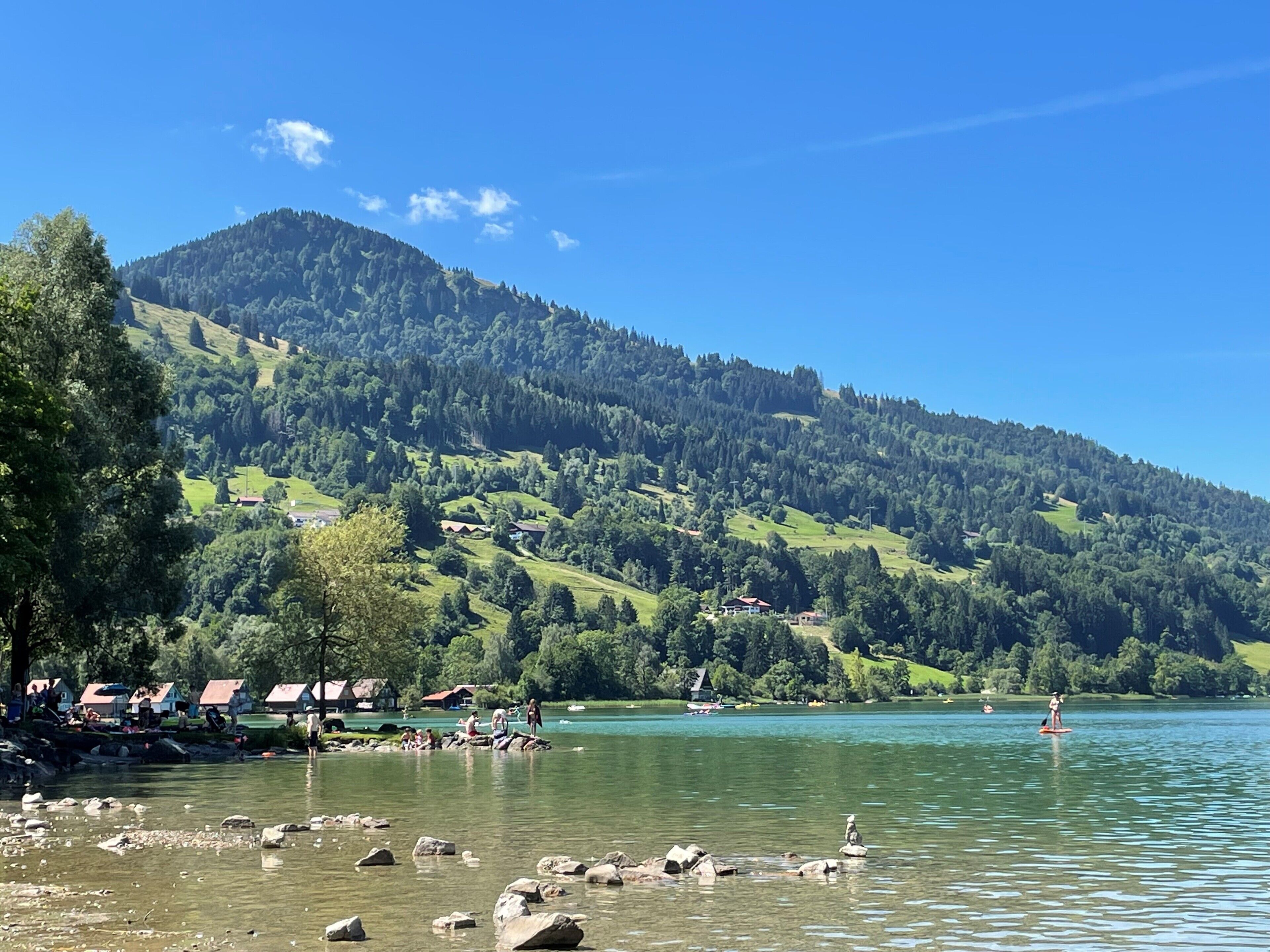 A lakeside view with a mountain in the background, clear skies, and a few buildings near the shore.