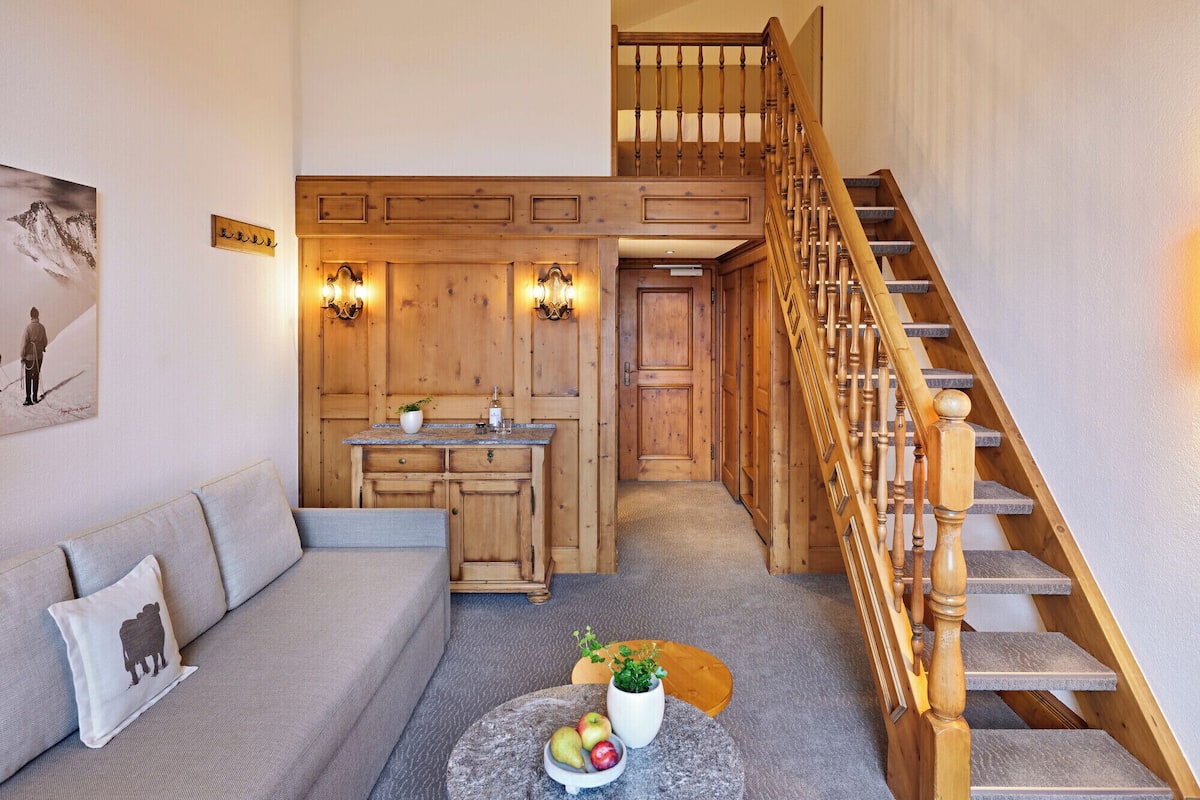 A cozy living room with a wooden staircase, a sofa, a dining area, and a kitchen.