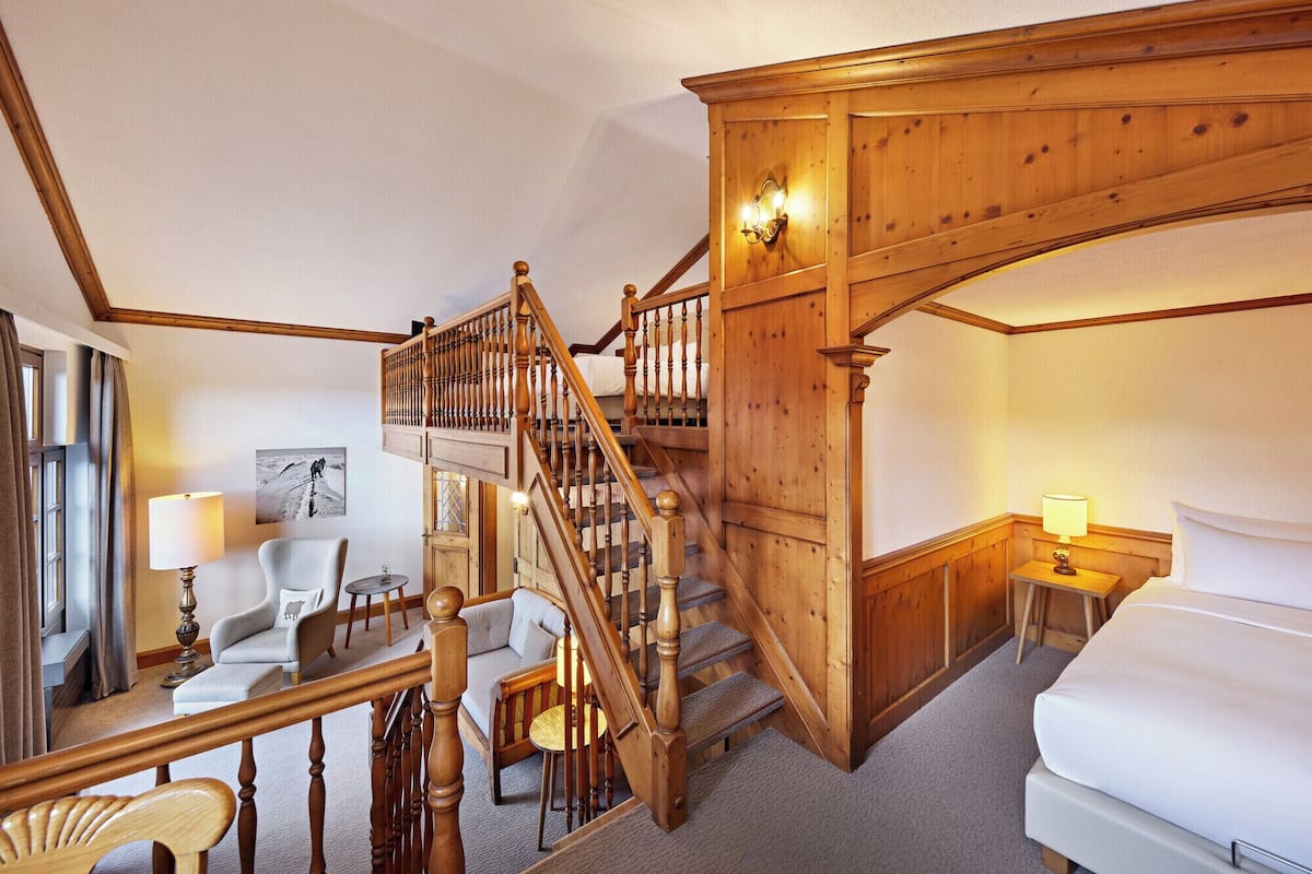 A wooden staircase with a railing, a bed, a chair, a lamp, and a painting on the wall.