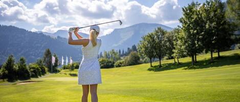 A person playing golf on a well-maintained course with a clear sky and mountains in the background.