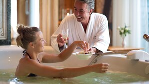 Een stel in een jacuzzi met een schaal eten en een glas wijn.