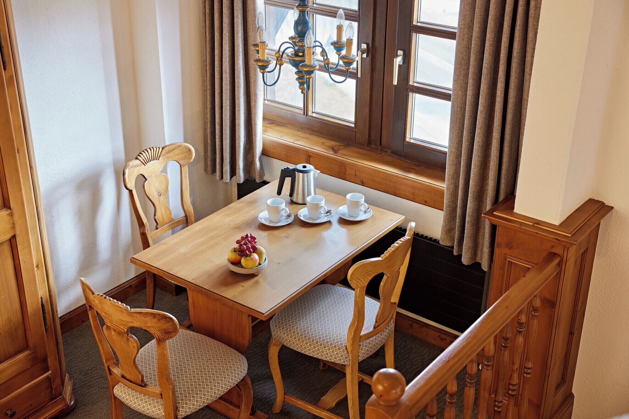 A wooden dining table with four chairs, a fruit bowl, and three white cups with saucers.