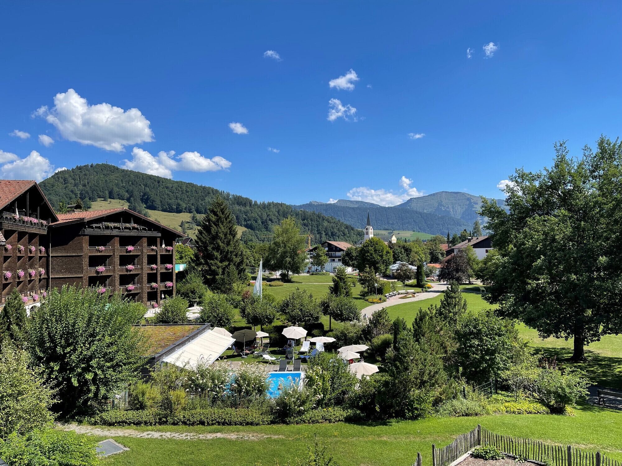 Un bâtiment traditionnel en bois, doté de balcons, entouré d’une végétation luxuriante et surplombé d’un ciel bleu azur.