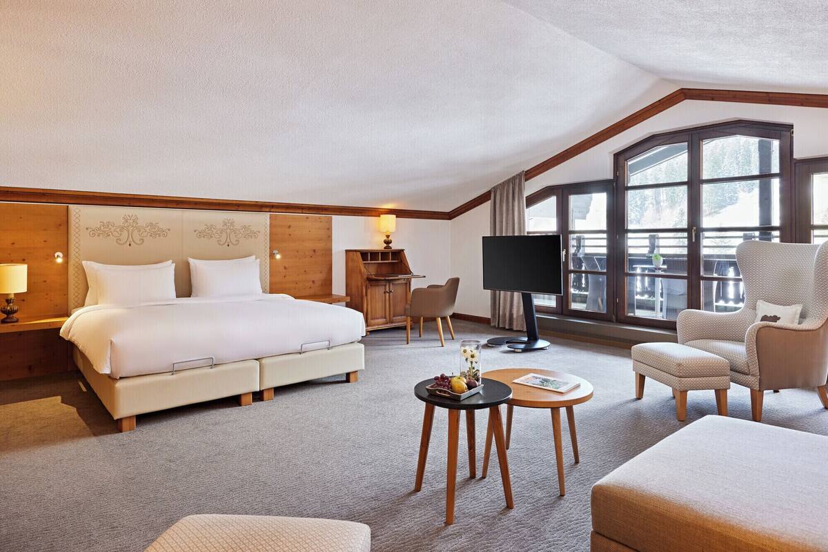 A hotel room with a large bed, a TV, a desk, and a balcony with a view.