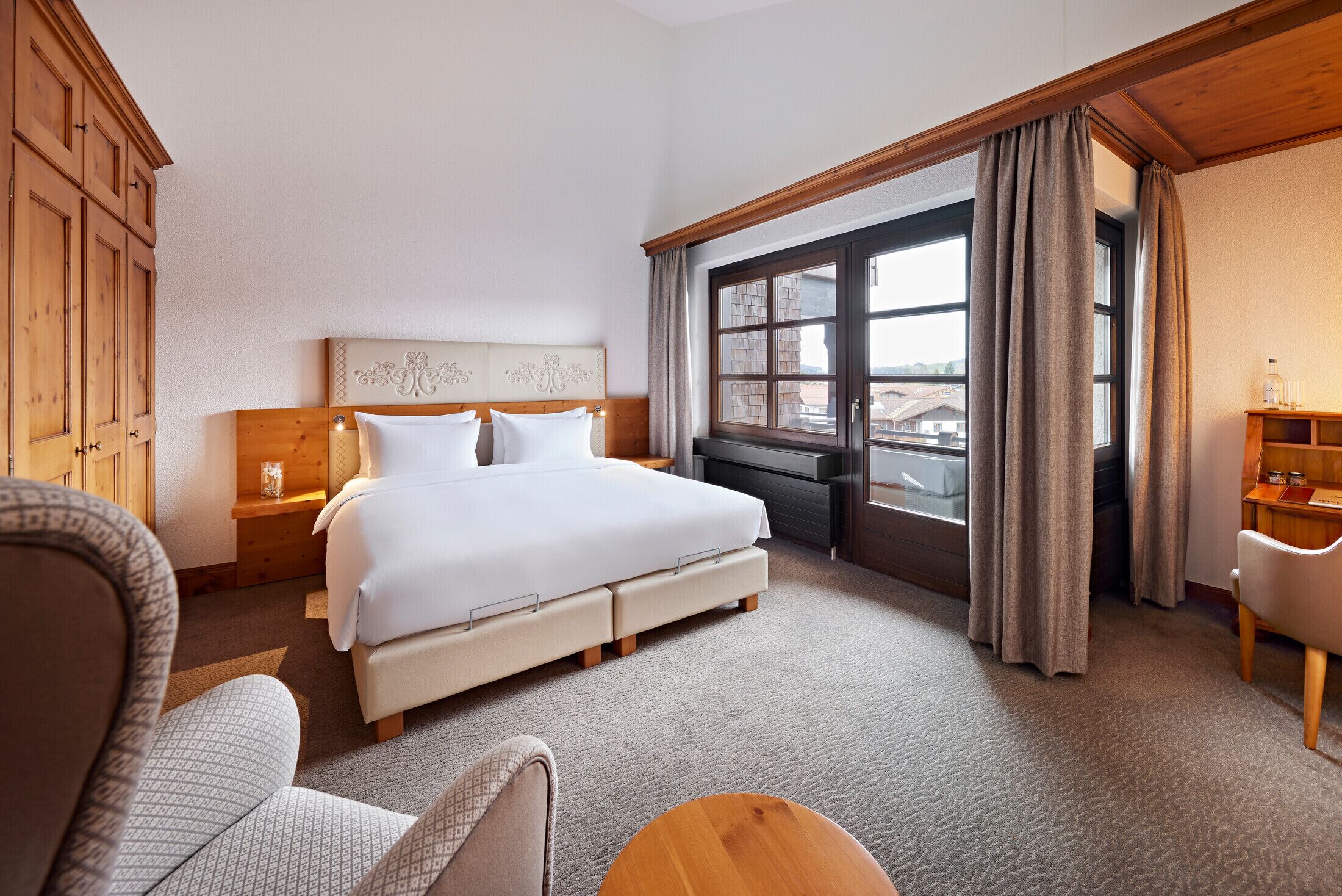 A hotel room with a large bed, a wooden headboard, a desk, a chair, and a window with curtains.