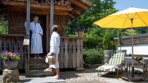 Een houten vakantiehuis met een veranda, een gele parasol en buitenzitplaatsen.