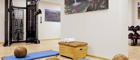Un gimnasio con equipo de ejercicio, colchonetas azules, cajas de madera y una pintura de cascada.