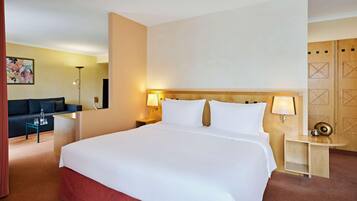 A hotel room with a large bed, bedside tables, a desk, a sofa, and a lamp.
