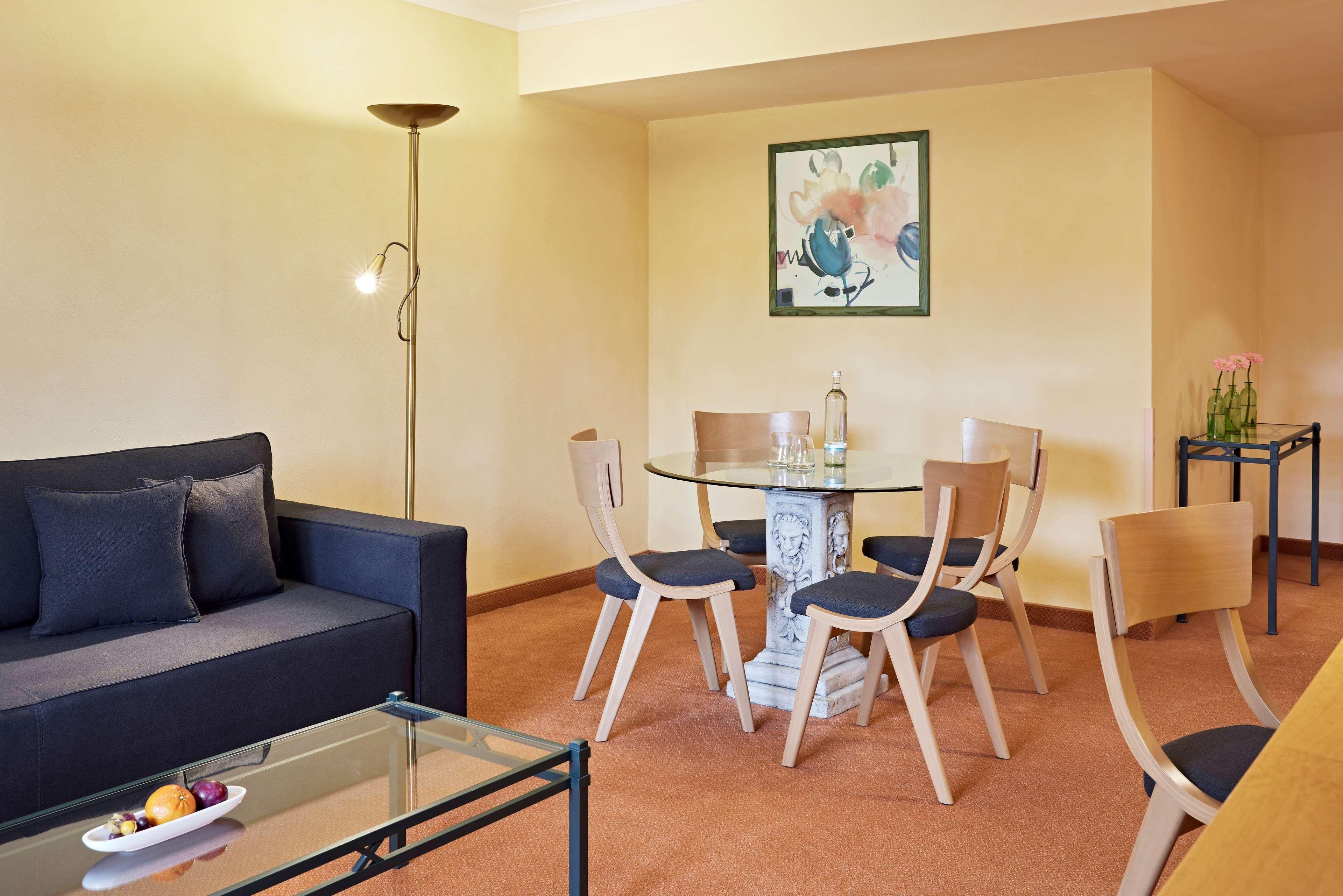 Una sala de estar moderna con un sofá, una mesa de centro de vidrio, una mesa de comedor con sillas y una lámpara de pie.