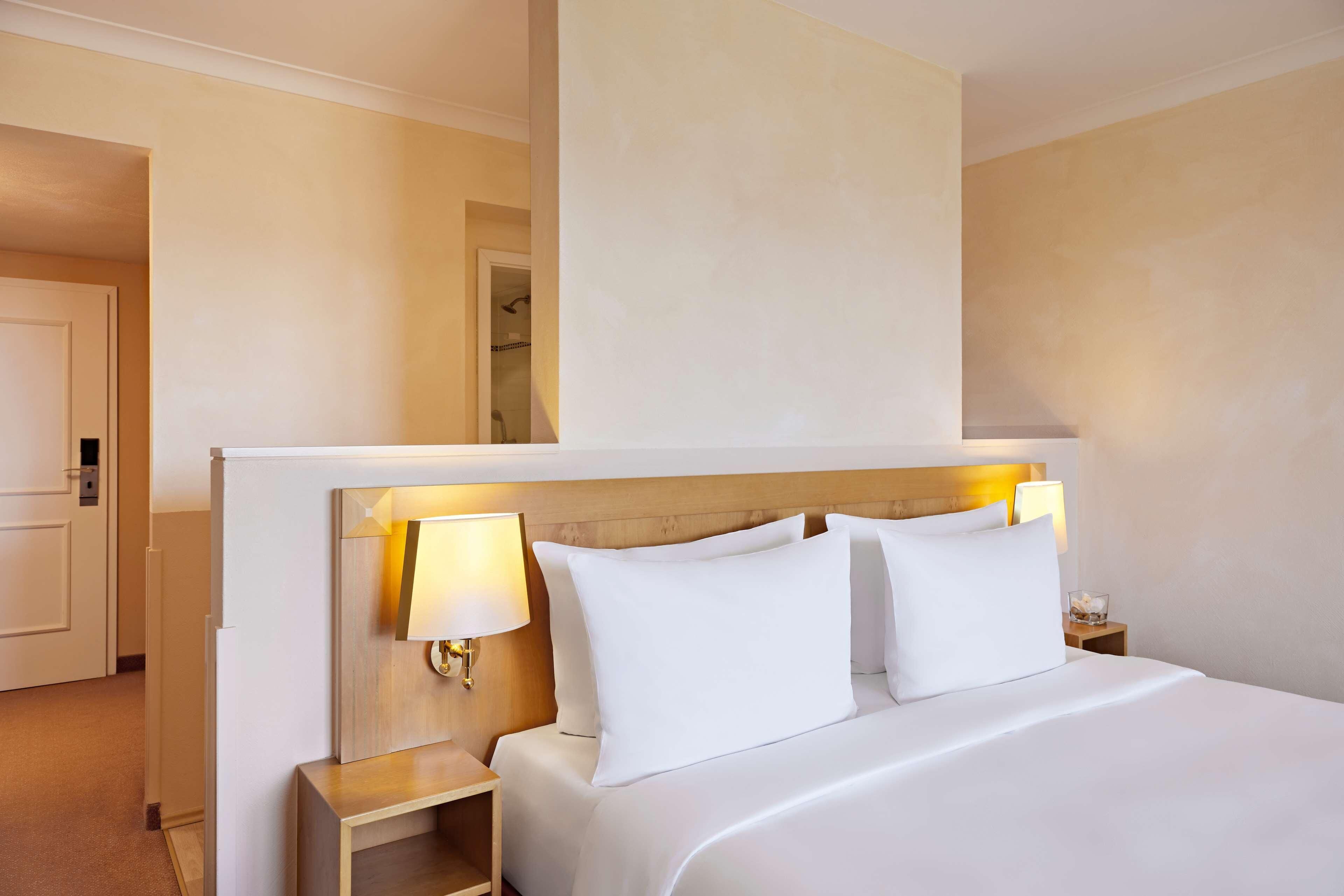 Ein Hotelzimmer mit einem großen Bett, zwei Nachttischlampen, einem hölzernen Kopfteil und einem Nachttisch mit einem Glasbehälter.