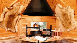 Interior d'una cabana de fusta amb una taula central, catifes de pell penjades i una gran làmpada negra suspesa.