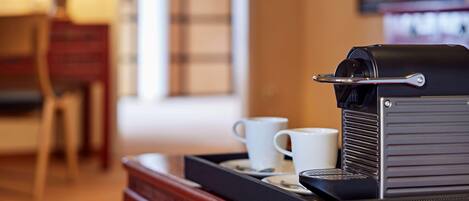 Una cafetera sobre una bandeja con dos tazas blancas, una mesa de madera y una lámpara al fondo.
