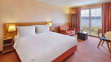A hotel room with a large bed, a chair, a table, and a view of a body of water through the window.