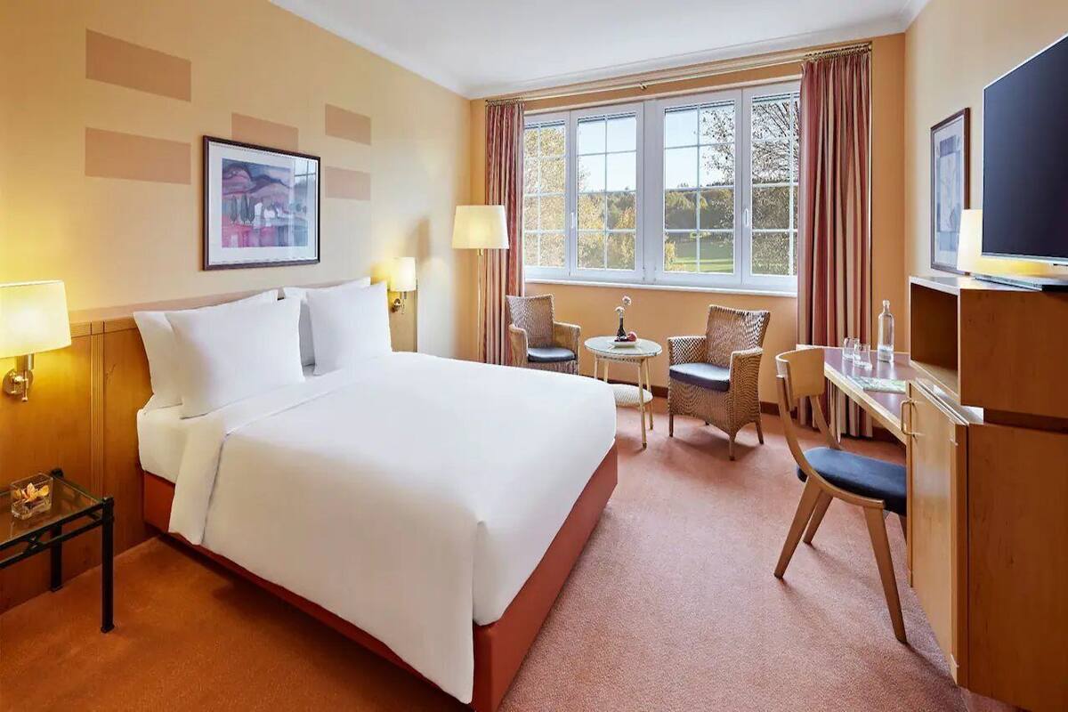 A hotel room with a large bed, two chairs, a small table, and a TV.