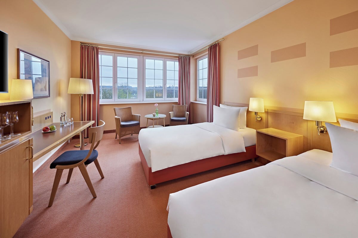 A hotel room with two beds, a desk with a chair, a small table with two chairs, and a TV on the wall.