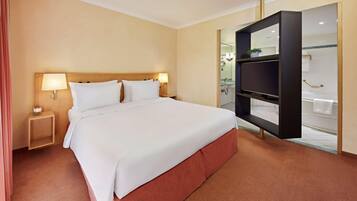 A hotel room with a large bed, bedside lamps, a TV, and a bathroom visible through an open door.