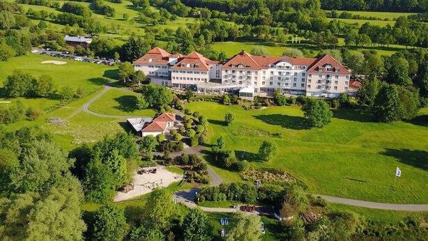 Un hotel gran amb diverses edificacions, envoltat de camps verds exuberants i un camp de golf.