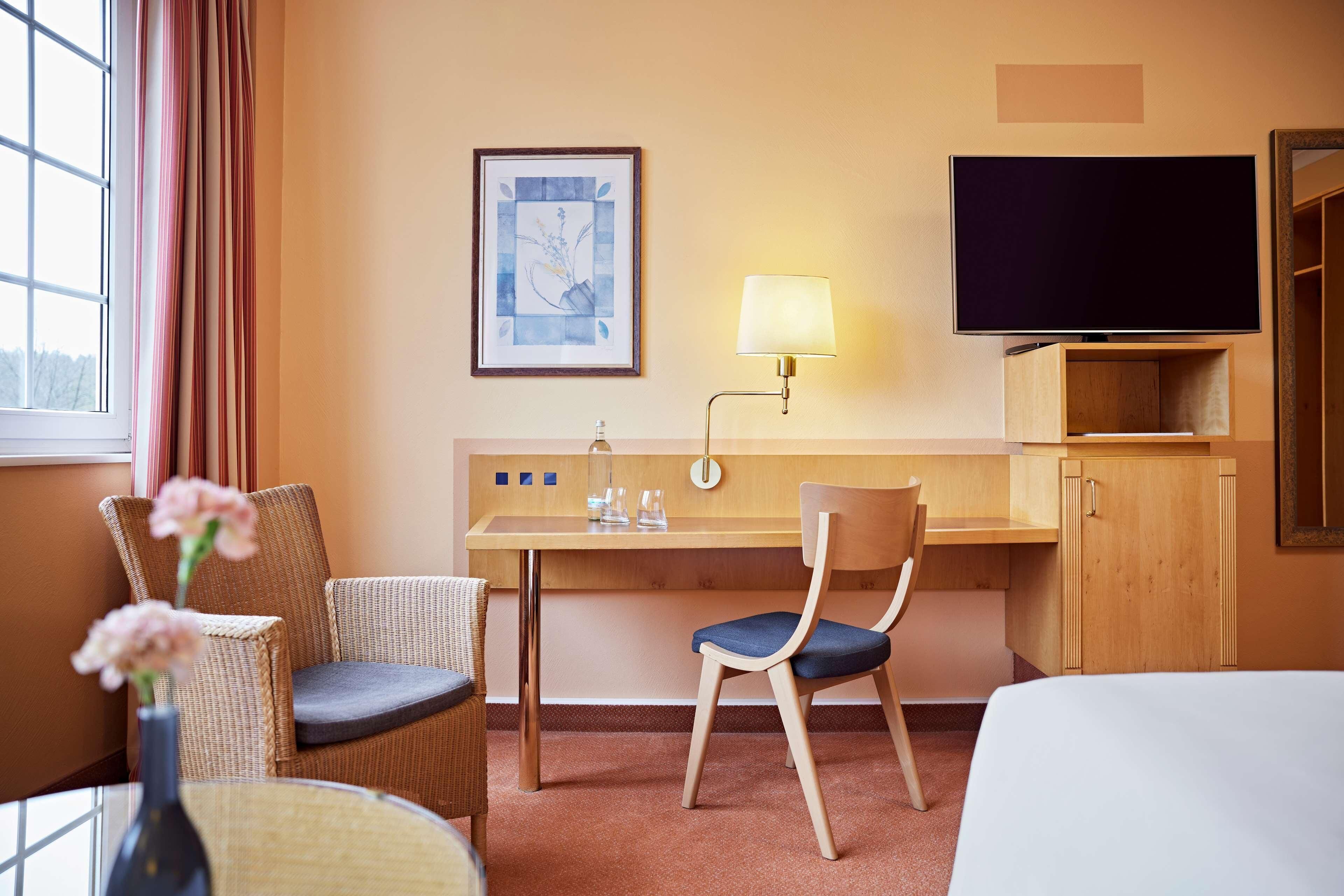 A hotel room with a bed, a desk, a chair, a TV, a lamp, and a framed picture on the wall.