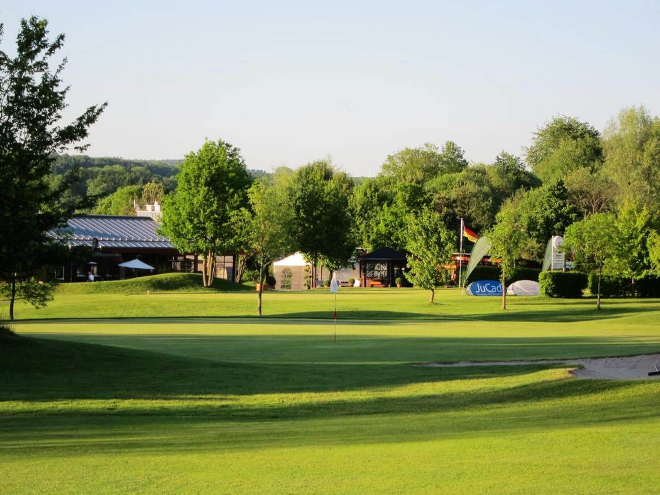 A golf course with a clubhouse, trees, and a clear sky.