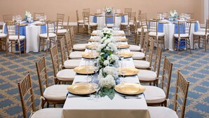 A banquet hall with long tables set for a formal event, featuring white tablecloths, gold chargers, and floral centerpieces.