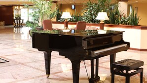 A grand piano in a lobby with marble flooring, two chairs, and a bench.