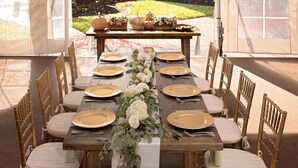 A tented dining area with a long table set for a meal, surrounded by wooden chairs.