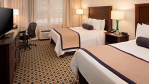 A hotel room with two beds, a desk with a TV, a chair, and a lamp.
