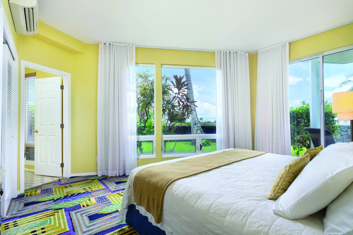 Une chambre avec un grand lit, une vue sur la verdure et un tapis à motifs.