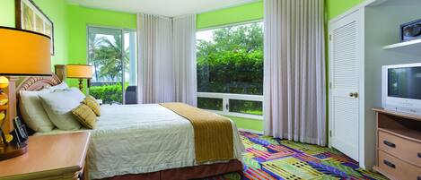 A hotel room with a bed, a television, a desk with a lamp, and a window with curtains.