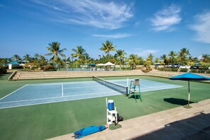 An outdoor tennis court with a net, surrounded by palm trees and umbrellas. - Holua Resort (Kailua-Kona)