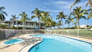 A swimming pool with a white fence, palm trees, and a building with a blue roof. - Holua Resort (Kailua-Kona)
