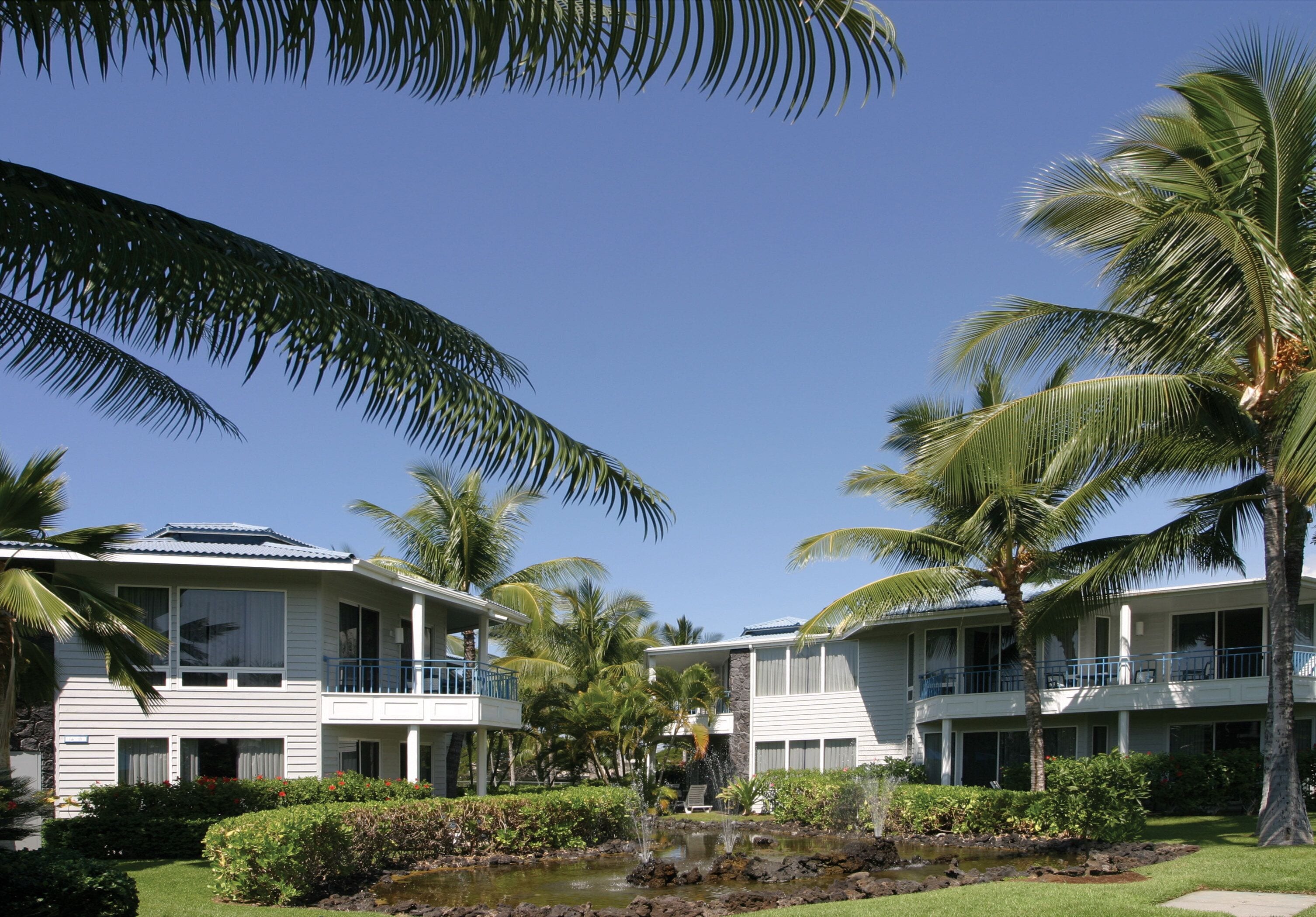 A resort with two-story buildings, a pool, and palm trees.