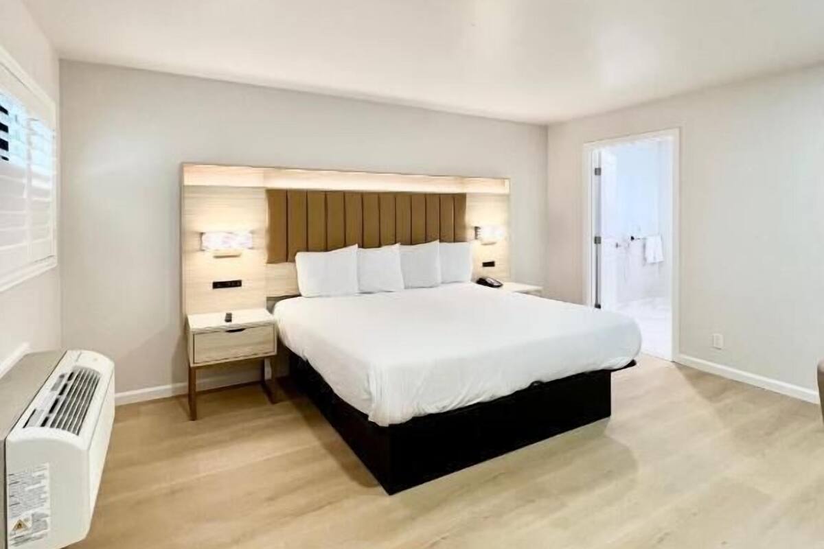 A modern bedroom with a large bed, bedside tables, a wall-mounted heater, and a door leading to a bathroom.