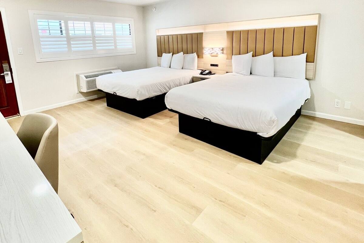 A hotel room with two beds, a desk, and a window with blinds.