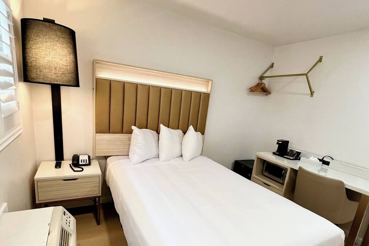 A hotel room with a large bed, bedside table with a lamp, a desk, and a wall-mounted TV.