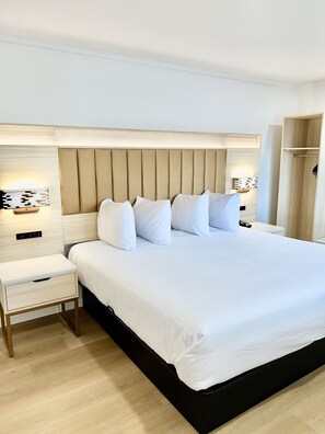 A neatly made bed with white linens and a wooden headboard, a bedside table with a lamp, and a wardrobe to the right. - Francisco Bay Inn (San Francisco)