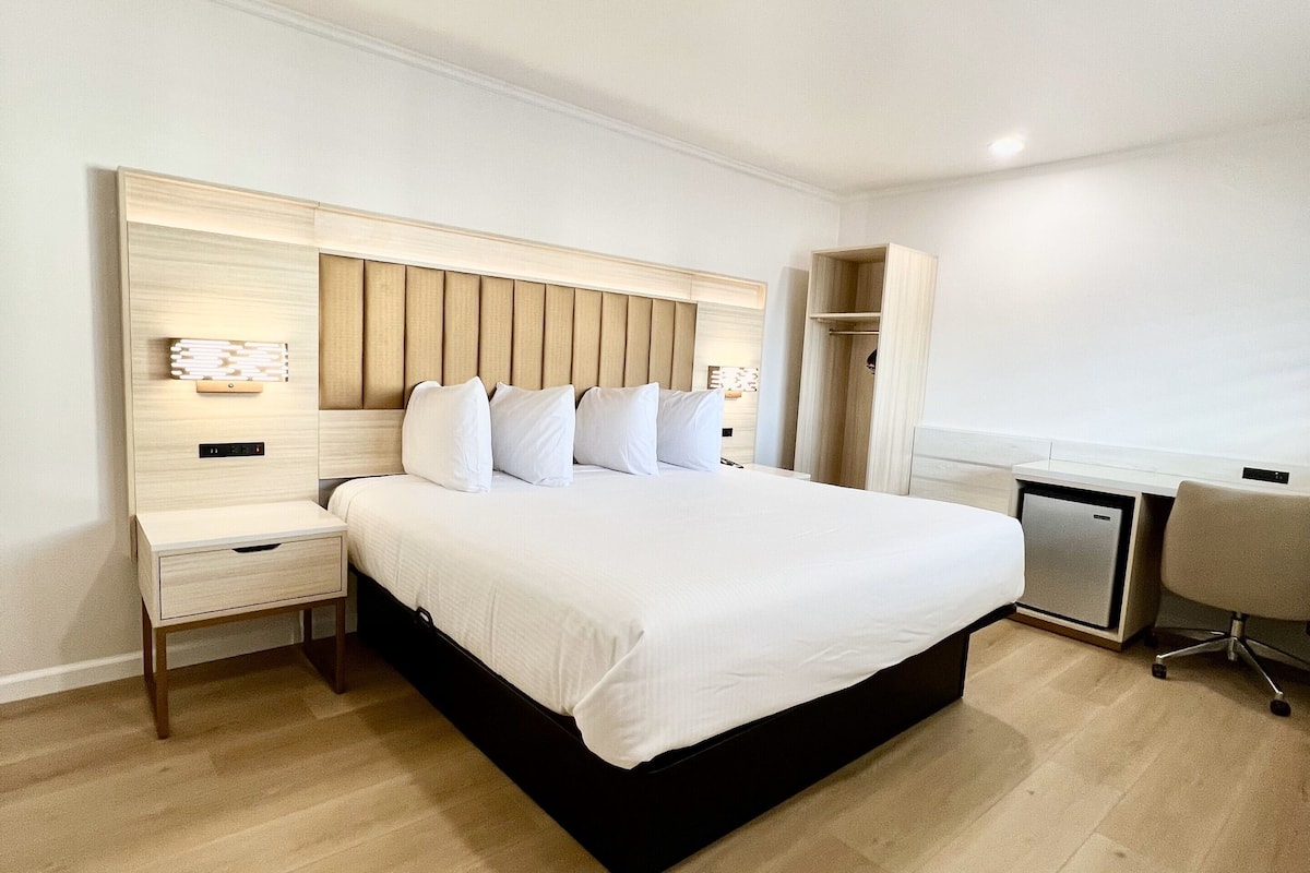 A modern hotel room with a large bed, bedside tables, a desk, and a chair.