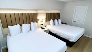 A hotel room with two beds, a wooden headboard, a bedside table with a lamp, and a door.