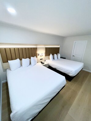 A hotel room with two beds, a wooden headboard, a bedside table with a lamp, and a door. - Francisco Bay Inn (San Francisco)