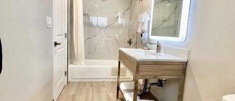 A modern bathroom with a bathtub, a vanity with a mirror, and a toilet.