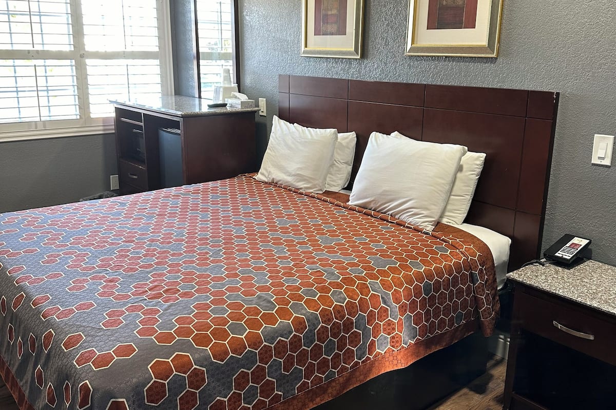 A hotel room with a large bed, a nightstand, a desk, and a window with blinds.
