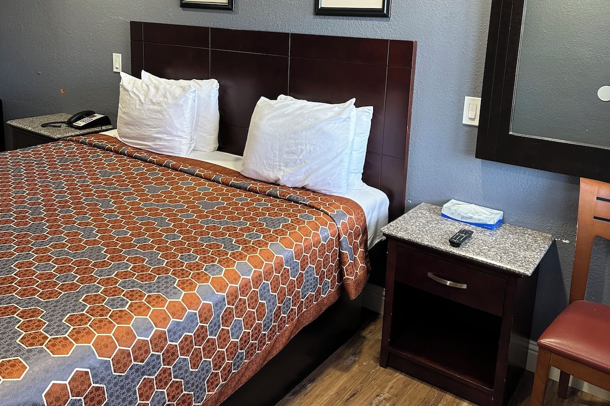 A hotel room with a bed, a nightstand, a desk, a chair, and two framed pictures on the wall.