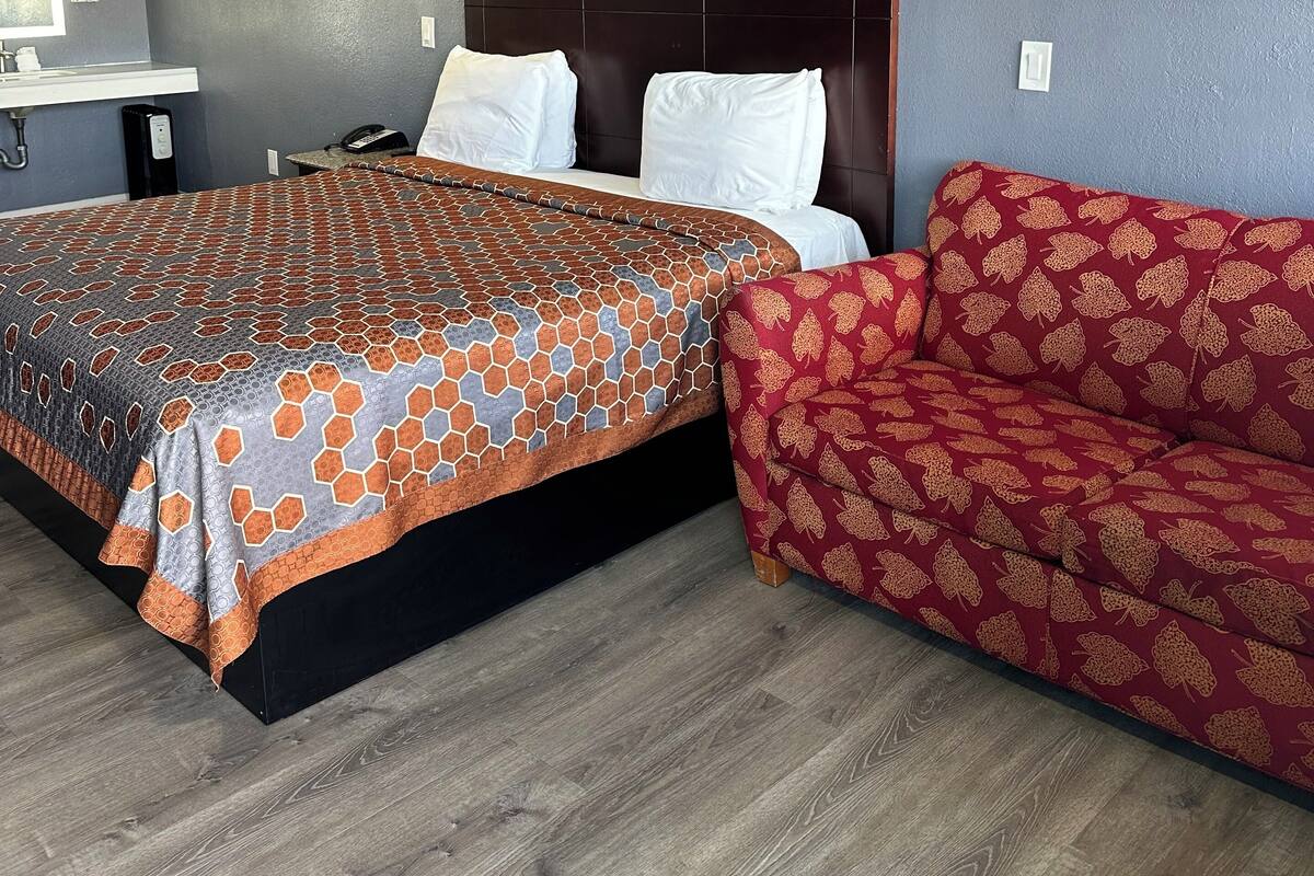 A hotel room with a bed, a sofa, a painting, and a desk with a phone.