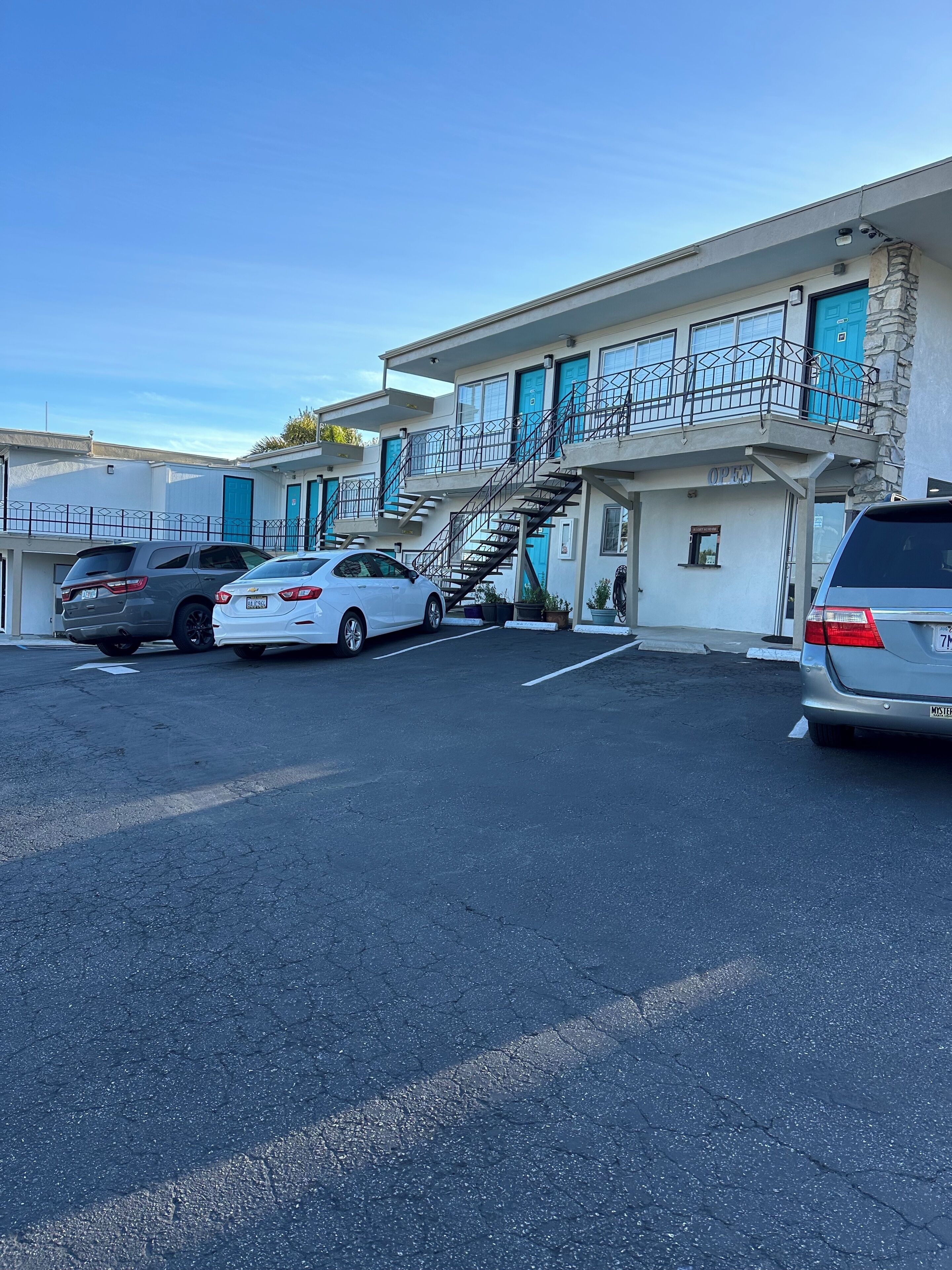 A motel with a parking lot, multiple cars parked, and a staircase leading to the entrance.