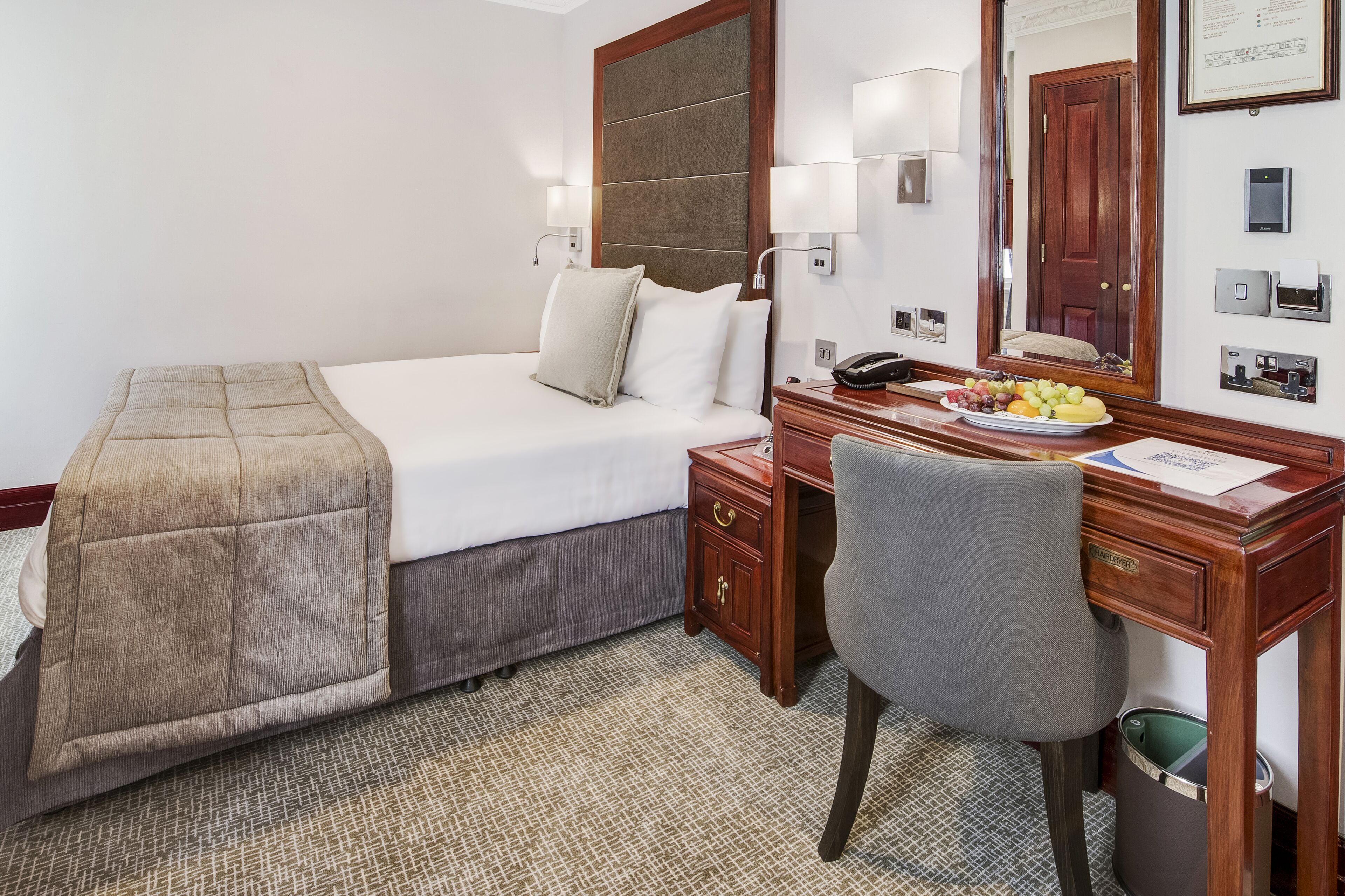 A hotel room with a bed, bedside table, desk, chair, and a mirror.