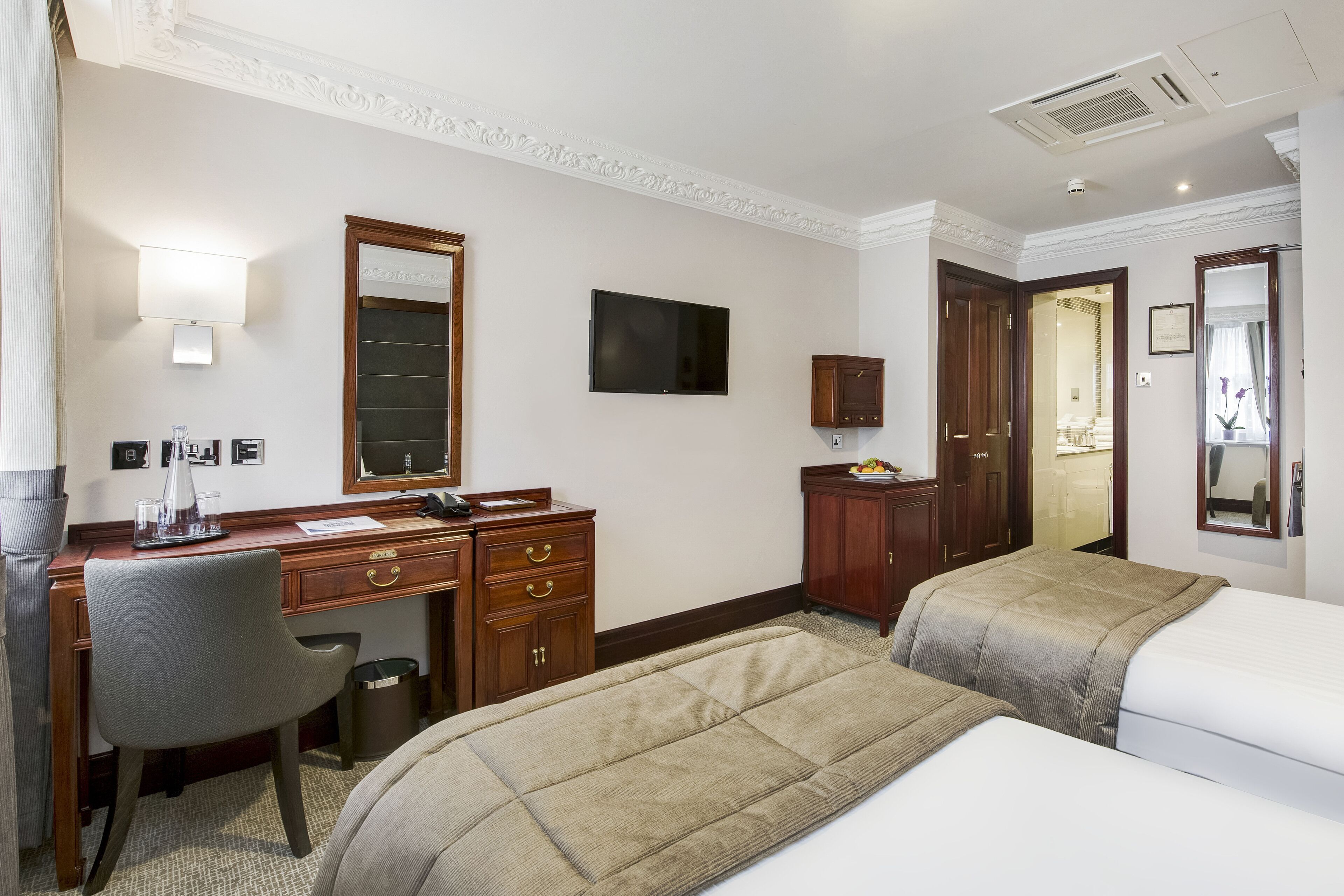 A hotel room with a desk, two beds, a TV, a mirror, and a wardrobe.
