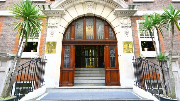 A building with a grand entrance, featuring a large arched doorway with glass panels and wooden doors, flanked by two palm trees.