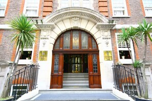 Un edificio con una entrada imponente, que presenta un amplio arco con paneles de vidrio y puertas de madera, flanqueado por dos palmeras.